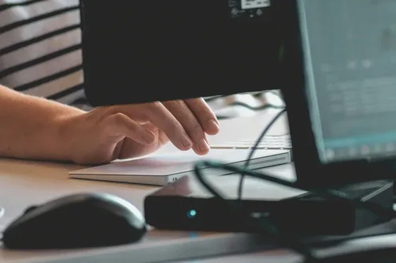 Close-up of a hand at a desktop keyboard with the monitor and mouse visible to the side