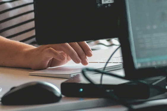 Close-up of a hand at a desktop keyboard with the monitor and mouse visible to the side