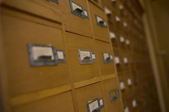 Rows of wooden card-catalog drawers with brass label holders in a library archive setting
