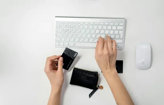 Overhead view of hands holding a credit card next to a wireless keyboard and a small leather card wallet
