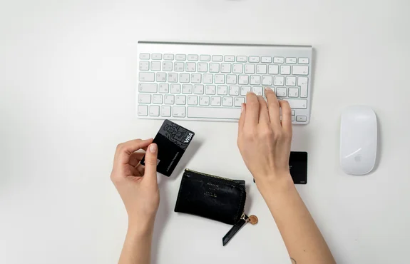 Overhead view of hands holding a credit card next to a wireless keyboard and a small leather card wallet