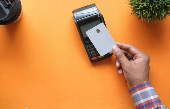Overhead view of a hand inserting a chip card into a payment terminal on an orange surface